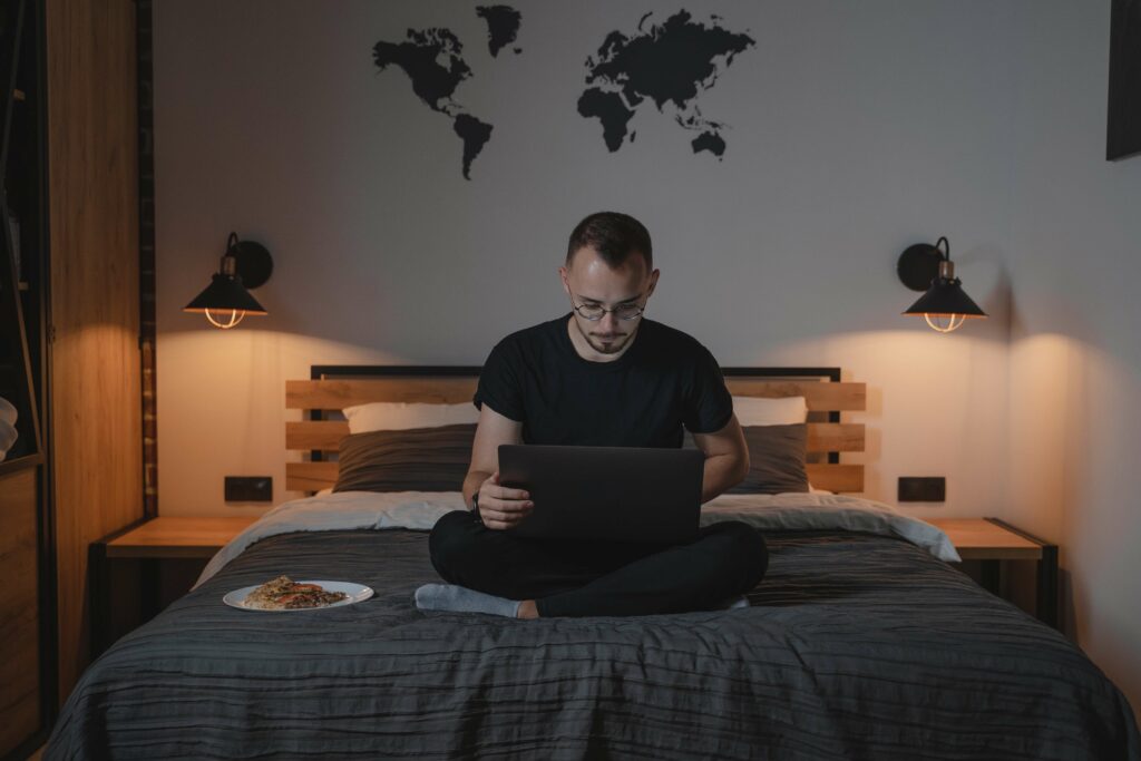 Man looks at his laptop while in bed as he is focused in working remotely.