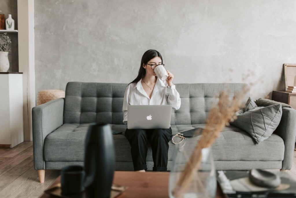Woman drinks coffee in a sofa as she is focused in working from home.
